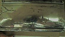 Coperchio in argento della scatola-teca in radica che commemora la partecipazione alla battaglia aereo-navale di Punta Stilo. Sul bordo superiore i dettagli storici, sul bordo inferiore la descrizione degli eventi a bordo.