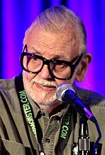 The image depicts horror director George A. Romero speaking at an event in Phoenix, Arizona.