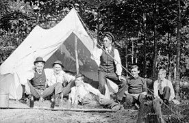 Photo noir et blanc, vers 1907 ; six hommes posent devant une toile de tente installées sous des arbres.