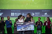 S.M. la Reina Doña Letizia hizo entrega de un “simbólico billete” a la ganadora de la cuarta edición nacional de Famelab, la bióloga Alba Aguión que le llevó a representar a España en la final internacional de monólogos científicos del Cheltenham Science Festival que se celebró en junio de 2016.