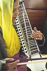 Mujer en una pashmina amarilla tocando un instrumento.