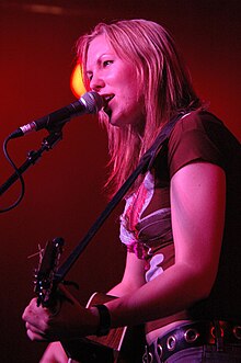 Thea Gilmore standing onstage, singing into a microphone and playing an acoustic guitar