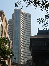 A skyscraper with curved walls and glass panes. A round building and a tree seen on its right side