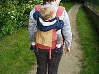 Woman wears an ERGO baby carrier on her back, a popular brand of soft structured carrier.