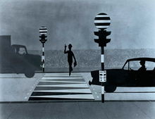 A black and white illustration showing a man crossing the road at a Panda crossing, jauntily raising his hat to the vehicles which are stopped