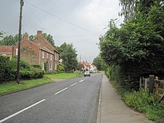 A rural street with house on the left, and hedges and trees on the right