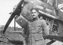 Photographie noir et blanc d'un homme en uniforme devant un avion à hélice.