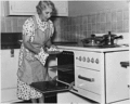 Elderly lady removes pie from oven (Rural Electrification Administration)