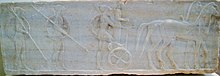 Sculpture : deux hoplites à pied et un troisième montant sur un char.