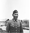 A man wearing a side cap, military uniform with an Iron Cross displayed at the front of his uniform collar.