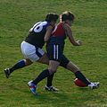 Melbourne University player bumps Darebin Falcons player off the ball in contest for possession over a ball on the ground from the 2007 Victorian Women's Football League Grand Final