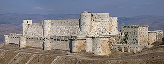 Photographie d'un imposant château fort composé de deux rangées de murailles situé dans un paysage vallonné recouvert de maquis