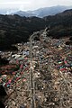 津波で壊滅的被害を受けた吉里吉里地区。画像中央を走る幅の広い道路は国道45号。山並みの向こうに見える煙は、大槌港の南側で発生した火災によるもの。3月15日撮影。