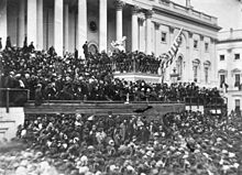 A large crowd in front of a large building with many pillars