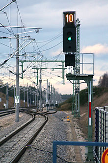 Das Bild zeigt ein Ks-Signal in Allersberg in der Funktion eines Hauptsignals. Zu sehen ist das Signal Ks 1 (ein grünes Licht) und darüber das Signal Zs 3 – Geschwindigkeitsanzeiger (eine weiß leuchtende Kennziffer), das eine 10 zeigt. Dieses Signal erlaubt die Fahrt mit 100 km/h.