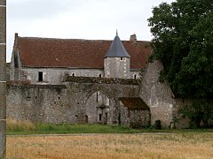 Vue générale d'un bâtiment dont la tourelle ronde dépasse d'un mur d'enceinte percé d'une porte cochère.