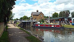 A picturesque river scene, with a deep-red canal boat in the centre and a black and white lock in the background.