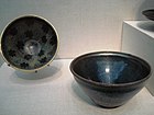 Two small polished black bowls. One has a large blue streak in it, the other has a polka-dot pattern on the inside consisting of black spots on a dark grey background. All of the coloring is created by features of the stone, rather than paint.