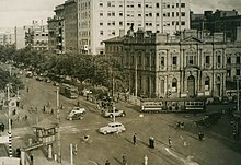 Electric trams and motor cars at a crossroads in a densely built up area