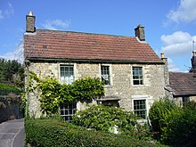 Two storey stone house with red roof. Partially obscured by vegetation