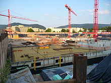 Trois grues rouges au-dessus d'un site de construction.