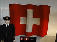 Schweizer Handelsflagge (rechteckig statt quadratisch aufgrund internationalem Seerecht), links im Bild Uniform