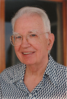 Coase looking to the camera and smiling, wearing a suit and tie