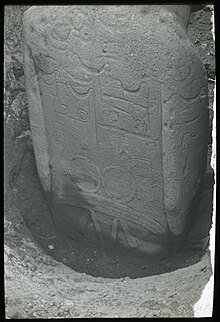 Photographie d'un moai à moitié enterré. Le dos de la statue est recouverte de motifs typiques des tatouages.