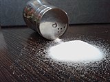 A small pile of white crystals in front of a tipped-over cylindrical with a few grains spilling out of the holes in its screw-top lid