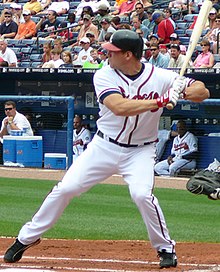 A man in a white baseball jersey prepares to swing at a pitch.