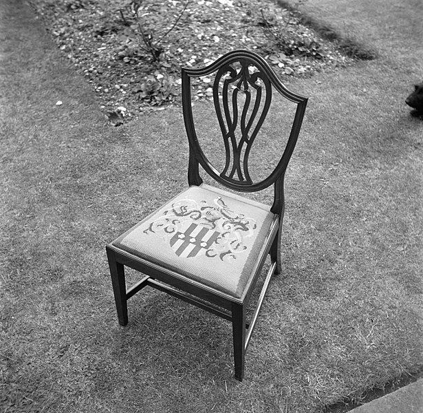 Close up of the seat of a wooden chair, embroidered with the coat of arms of the Martineau family