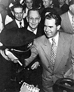 A smiling young man shakes hands; a Nixon bumper sticker is seen.