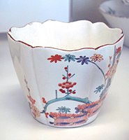 一个圆形瓷杯，杯口呈微微波浪形，杯身绘有植物。