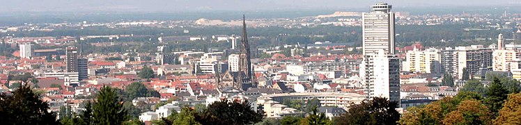 Vue panoramique de la ville de Mulhouse depuis la tour du Belvédère (quartier du Rebberg, secteur 2). On distingue au centre le temple Saint-Étienne, à droite la tour de l'Europe – le seul gratte-ciel mulhousien correspondant aux critères d'Emporis – et au fond les terrils du Bassin potassique et la forêt de Nonnenbruch.