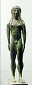 Estatuilla votiva realizada en bronce, de un joven desnudo con los brazos a los lados, proveniente de Chiusi (550-530 a. C.).