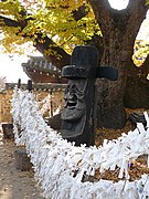 Photographie de deux statues en bois figurant deux visages. Devant eux pendent le long de fils de nombreux bouts de papiers.