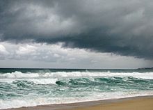 A beach is battered by choppy seas from an offshore storm and overcast, dark skies hang overhead.