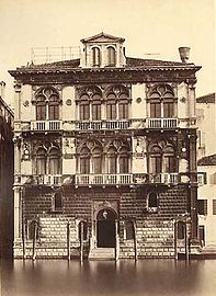 Image en noir et blanc de la façade d'un palais sur trois étages donnant sur un canal. Le rez-de-chaussée est en pierre de taille avec un portail central, les étages supérieurs séparés par des corniches comportent des doubles fenêtres à meneaux à chaque étage, le toit est surmonté d'une mezzanine.