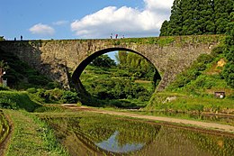 A large stone arch bridge that passes over a rice paddy.