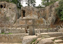 Mausolée circulaire en tuf entouré d'escaliers et directement taillés dans la pierre de la colline derrière.