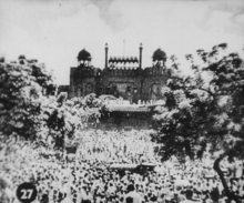 Numerous people gathered before the wall of a fort.