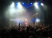 A woman standing on a stage and a man at a DJ booth.