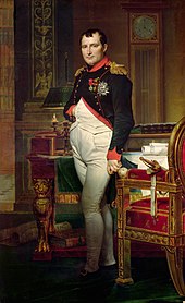 Napoléon debout, une main dans le gilet. Autour de lui, un bureau, un fauteuil, une pendule