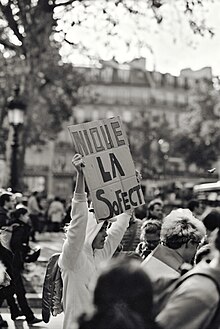 Photographie en noir et blanc d'une personne en onesie licorne tenant une pancarte en carton "nique la SoFECT"