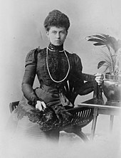 Photographie d'une jeune femme à la robe sombre assise sur une chaise.