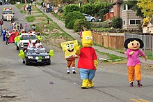 trois personnes défilent sur une route, déguisés en personnages issus de dessins animés.