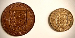 Fotografia przedstawia dwie monety z Jersey z czasów przed decymalizacją. Po lewej stronie zdjęcia znajduje się moneta o nominale 1/12 szylinga. Na jej rewersie, widocznym na zdjęciu znajduje się herb Jersey - trzy lwy oraz napis informujący o emitencie, dacie wybicia i nominale (Bailiwick of Jersey, 19-64, One twelfth of a shilling). Po prawej stronie zdjęcia znajduje się mosiężna moneta o nominale 1/4 szylinga. Na jej rewersie, widocznym na zdjęciu, podobnie jak przy monecie 1/12 szylingowej, znajduje się herb Jersey - trzy lwy oraz napis informujący o emitencie, dacie wybicia i nominale (Bailiwick of Jersey, 19-57, One fourth of a shilling