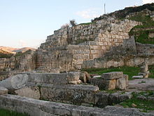 A wall made at its lower part of tightly packed white limestone stone blocks surmounted by a wall constructed of very large rusticated ashlar.