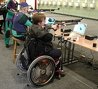 Tiro paralímpico co rifle em cadeira de rodas.