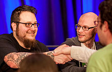 Edmund McMillen shakes hands with a person off-frame as Tommy Refenes looks towards him.